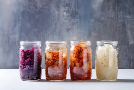 Vier glazen potten met gefermenteerde groenten: rode kool, kimchi en zuurkool